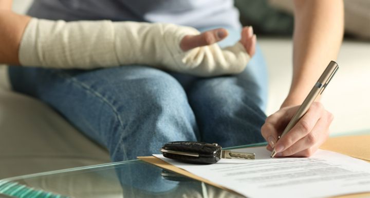 Woman with hand in bandage signing paperwork with car keys in foreground