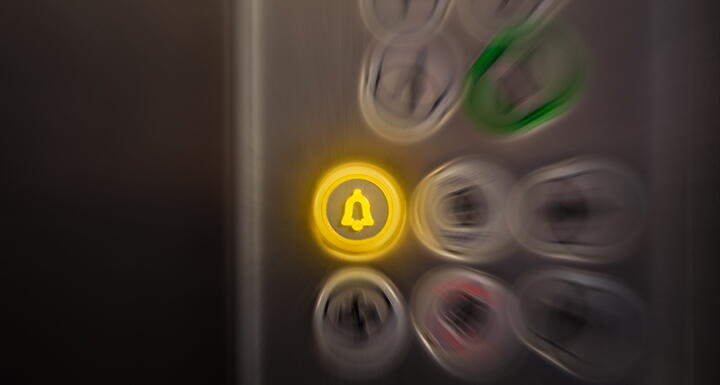 An alarm button lit in yellow in an elevator