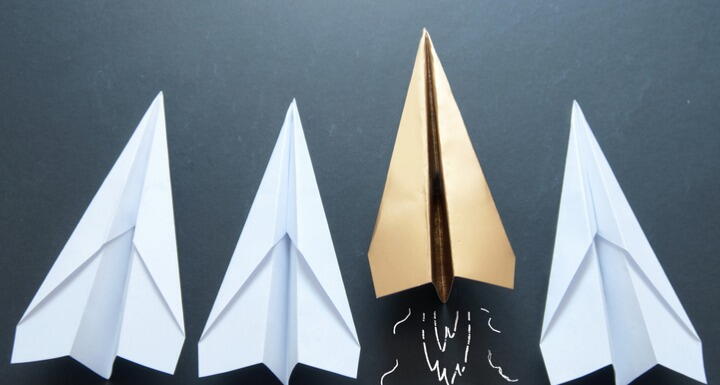 Gold paper airplane in between white paper airplanes