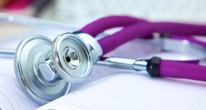 A stethoscope with a purple earpiece on a white lab coat